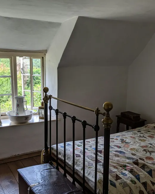 Chambre mansardée, lit en fer forgé et courtepointe colorée sous une fenêtre à petits carreaux