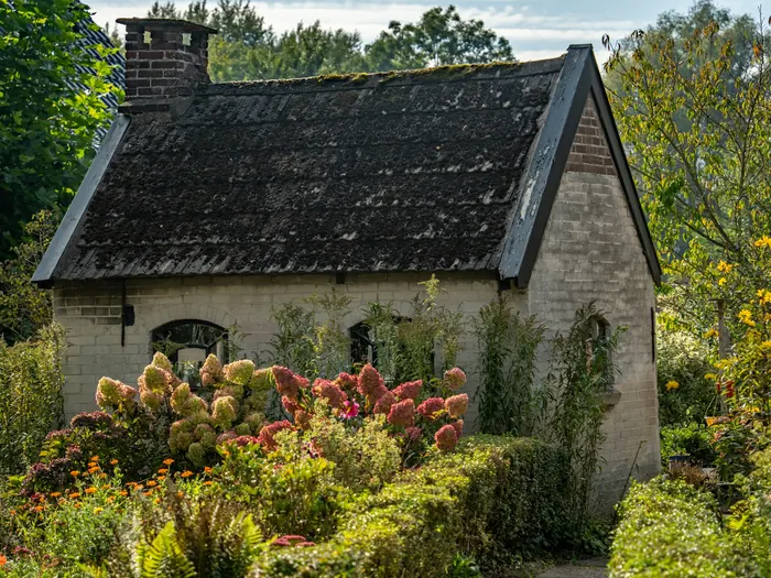 La longère de granit au toit d’ardoise, derrière un jardin en fleurs