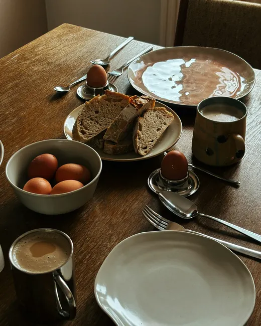 Table de bois au petit matin : œufs, pain au levain tranché, café dans des bols