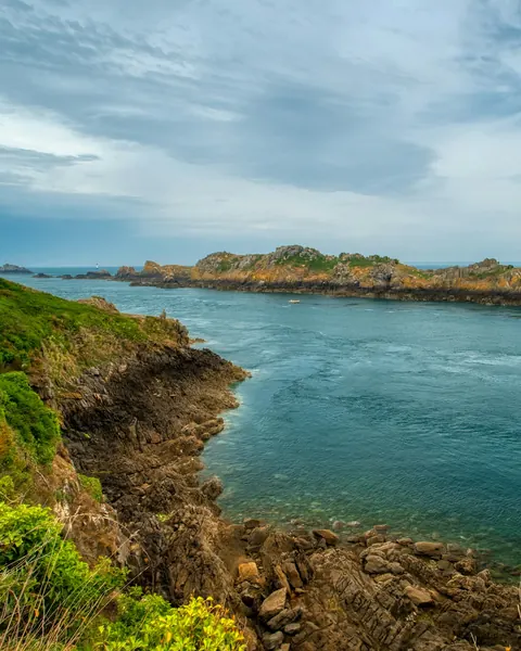 Côte herbue plongeant dans une eau verte, une île au loin