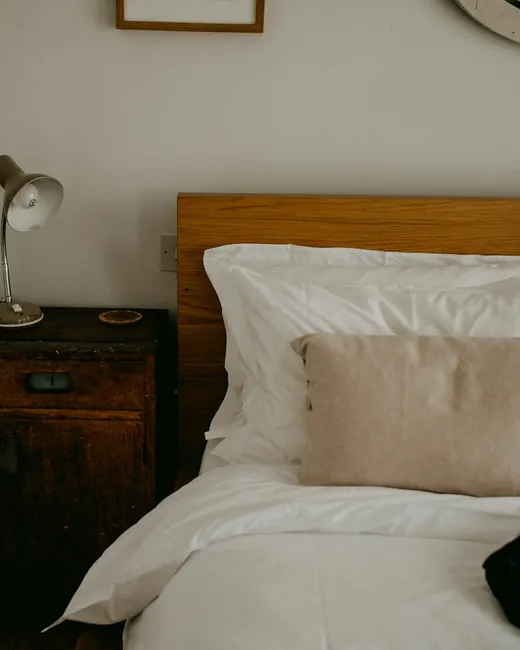 Lit aux draps blancs, tête de lit en bois blond et lampe de chevet ancienne