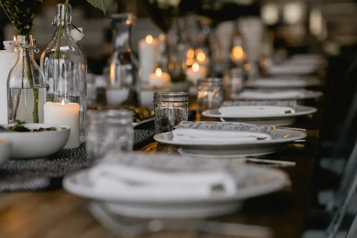 Longue table dressée, bougies allumées et bouteilles de verre
